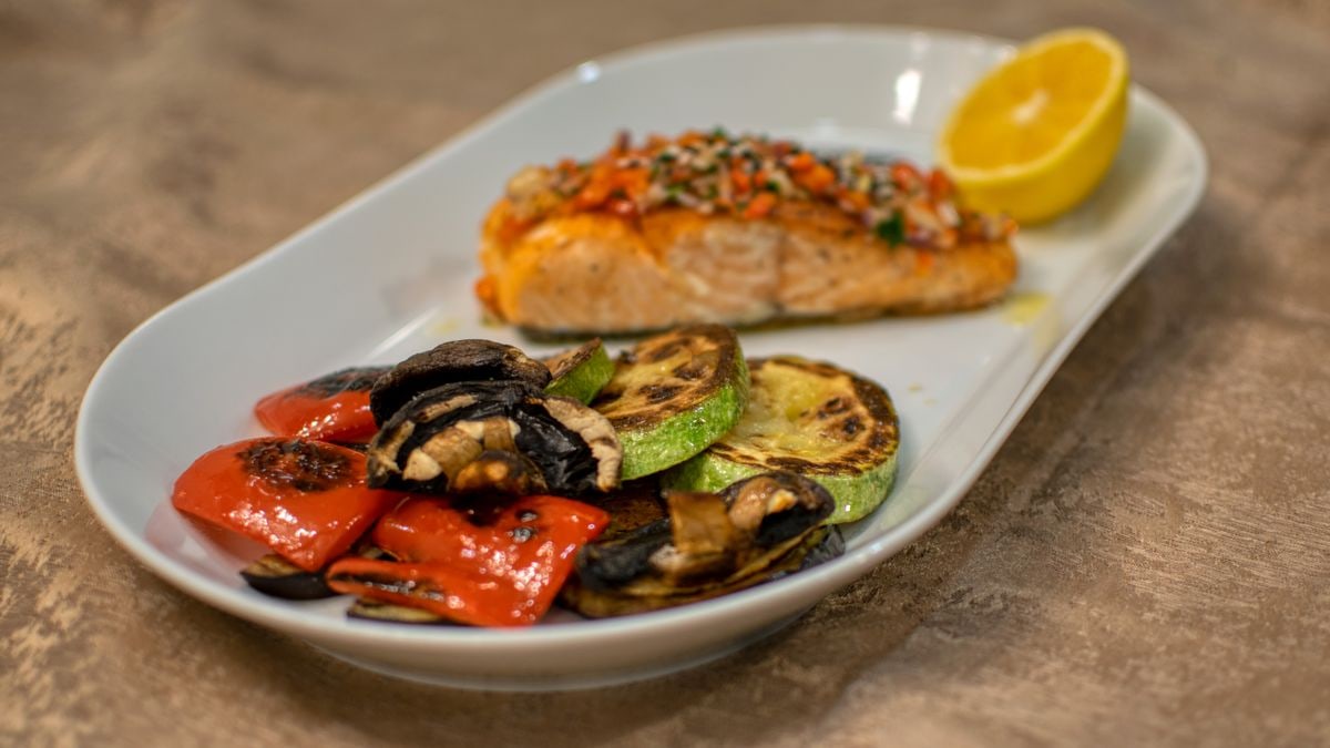 A delicious grilled salmon fillet with roasted vegetables served on a white plate.